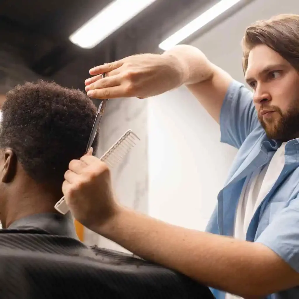 A barber skillfully trims a client's short, textured hair with scissors while holding a comb in the other hand, focusing on a precise Men's Crop & Crew Cut style.