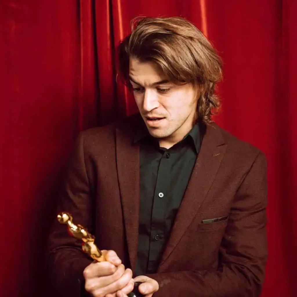 A man in a suit with curtain hair holding an award.