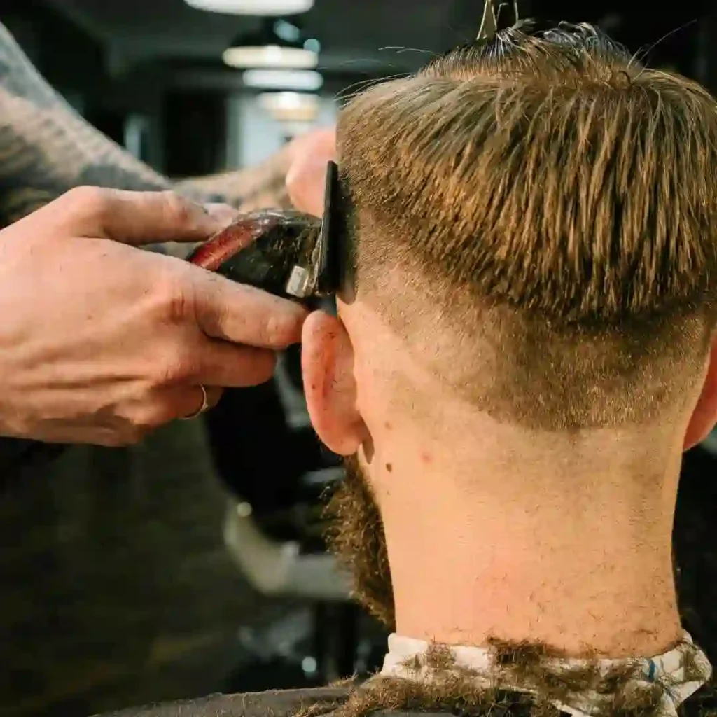 A barber trims the back of a man's head, using clippers to create a clean fade hairstyle.