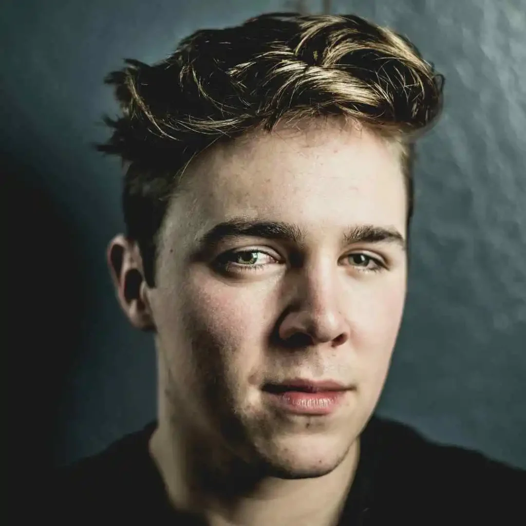 A close-up portrait of a person with stylish, tousled hair and a MEN HAIRSTYLES UNDERCUT, set against a textured dark blue background.
