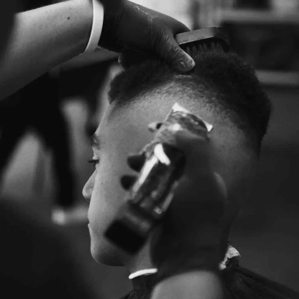 A barber styles a client's hair, using clippers on the sides while a comb is held in the other hand, creating a clean and sharp Men's Crop & Crew Cut, captured in black-and-white.