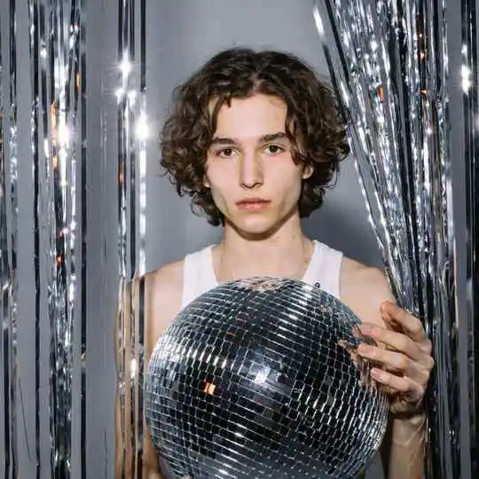 A man with curtain hair holding a disco ball in front of a mirror.