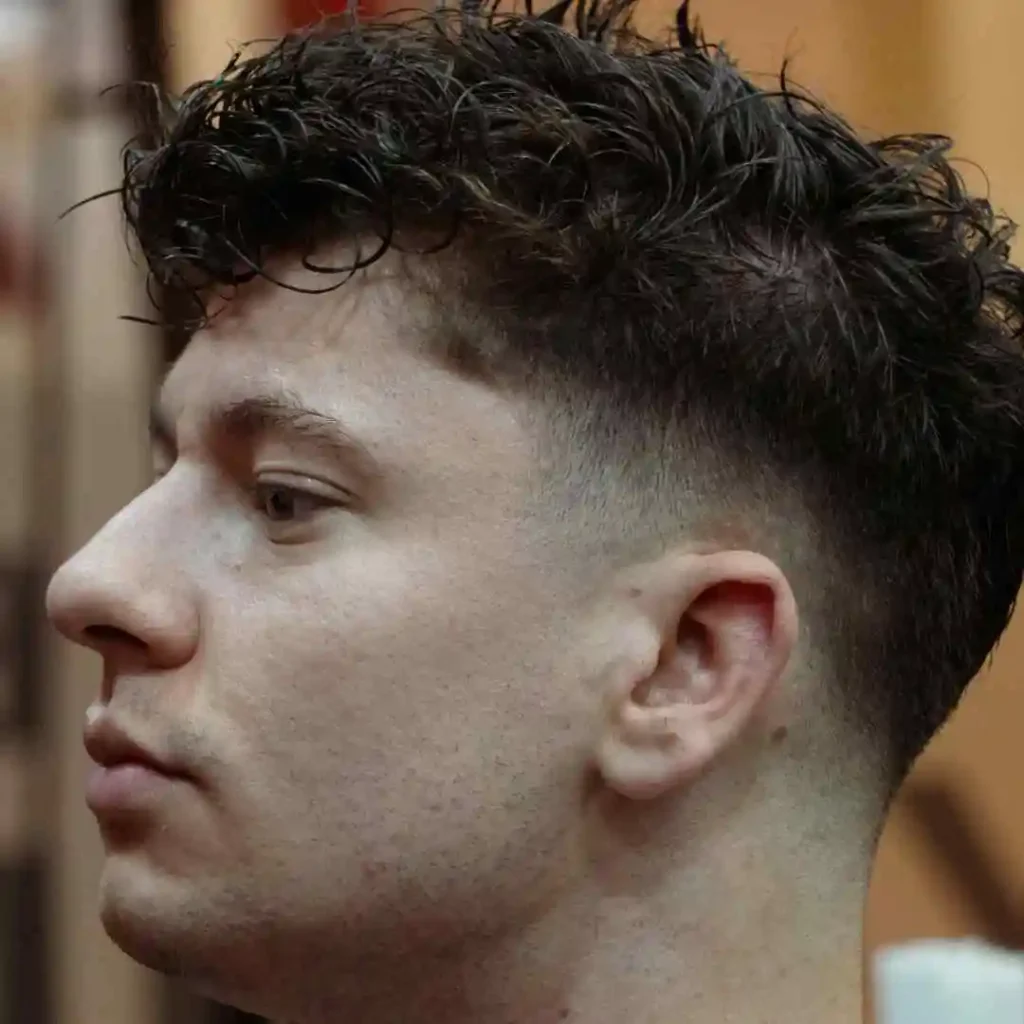 20 Trendy Options for Men Hairstyles Undercut 8 A close-up of a trendy, textured MEN HAIRSTYLES UNDERCUT featuring short sides and a voluminous, wavy top. The background is softly blurred.