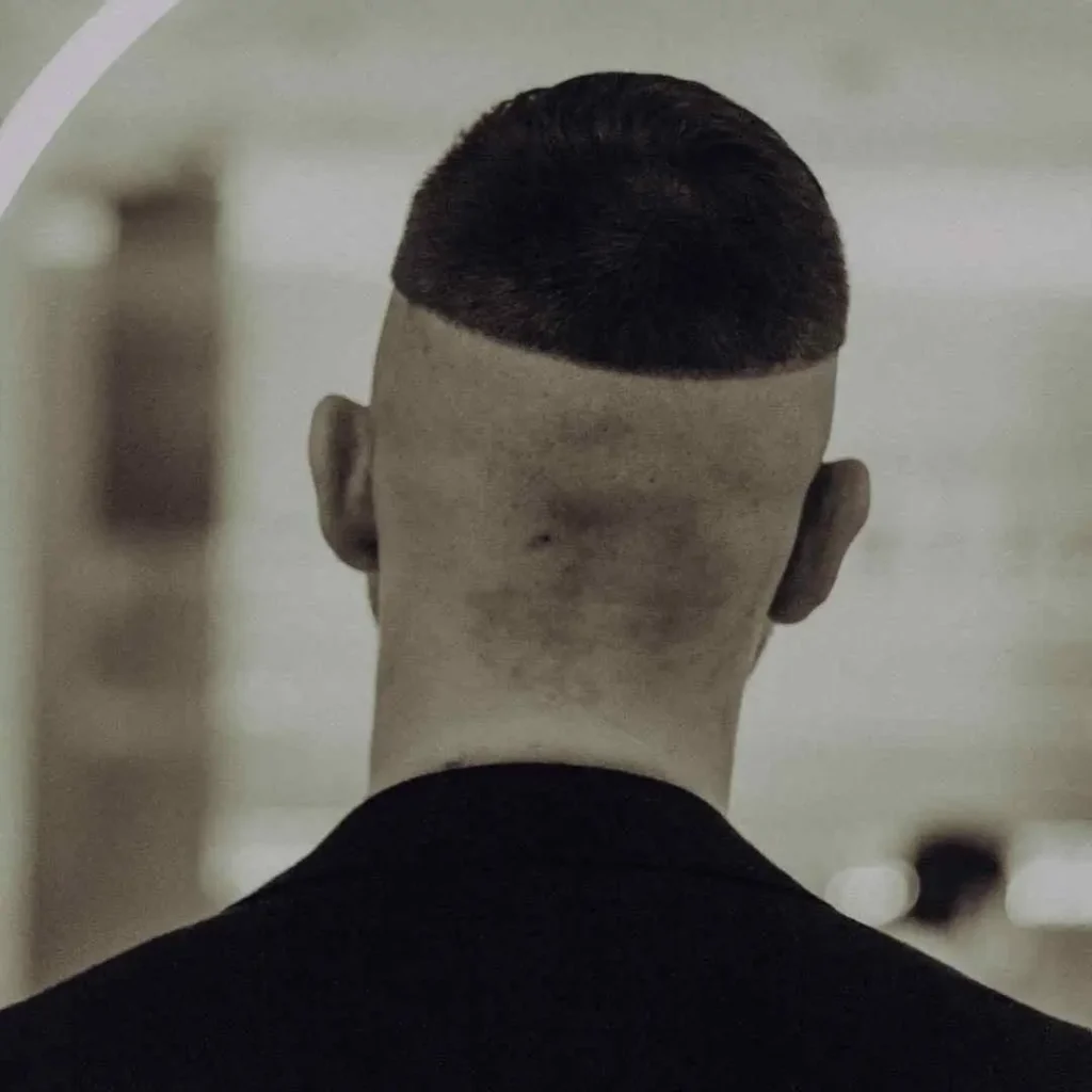 A close-up of the back of a person's head showing a distinct flat top haircut with closely shaved sides and neck.