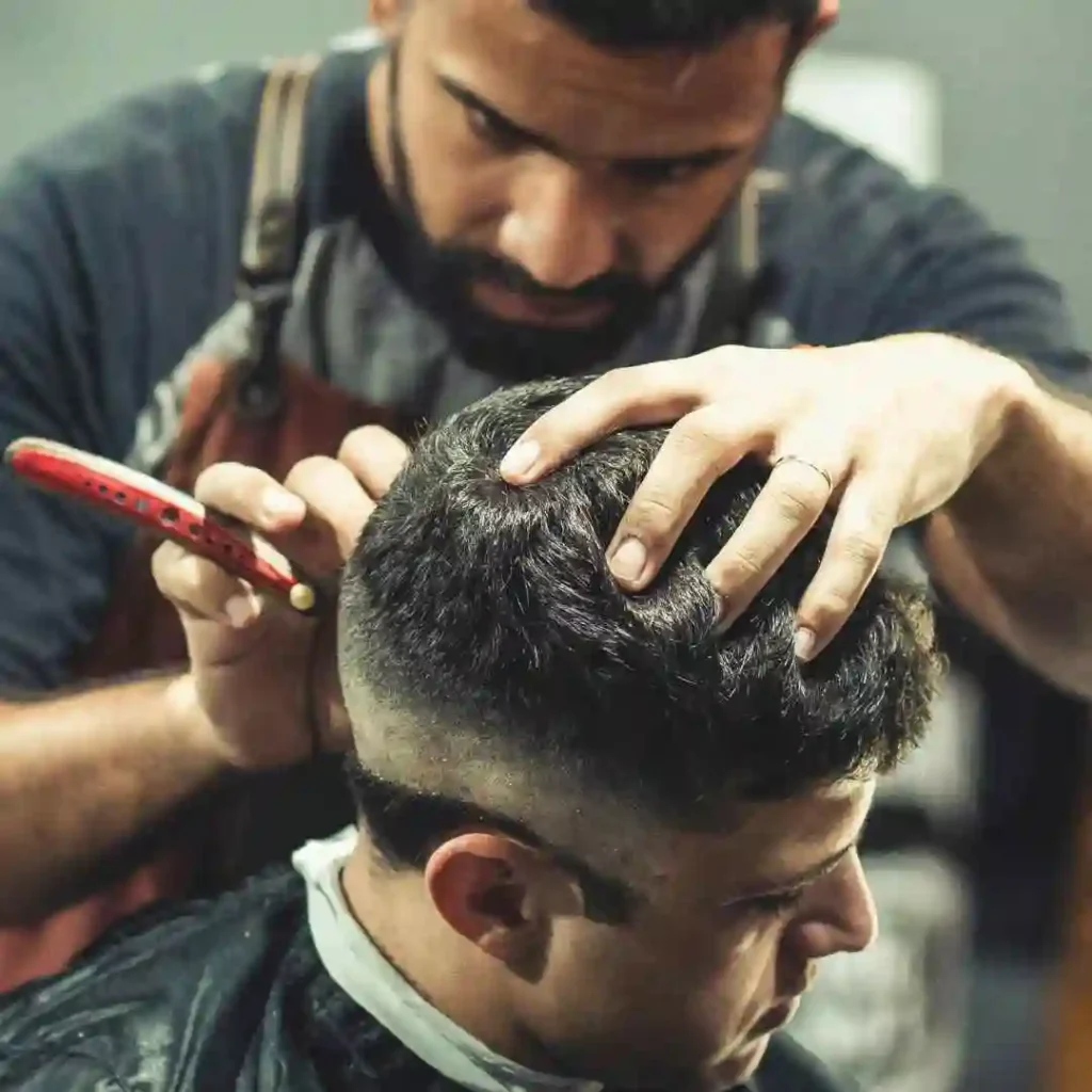 A man cutting another man's hair in a barber shop, focusing on styling a men's short curly haircuts.