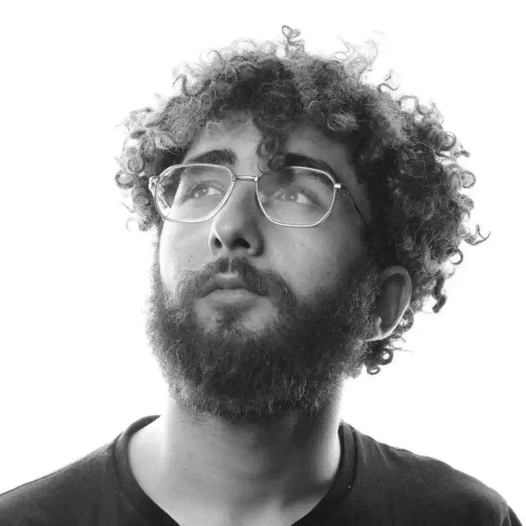 A man with curly hair and glasses looking up, showcasing a trendy men's short curly haircut.