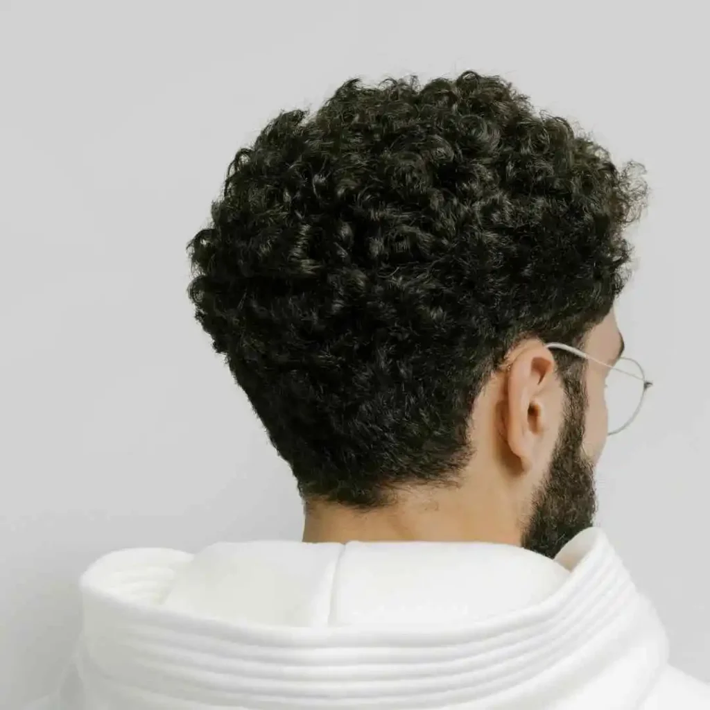 A man with a beard and glasses looking off into the distance, sporting a stylish men's short curly haircuts.