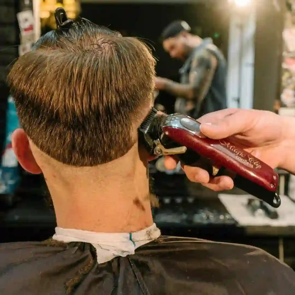 A barber trimming the back of a person's hair with electric clippers, focusing on a men’s hairstyle undercut.