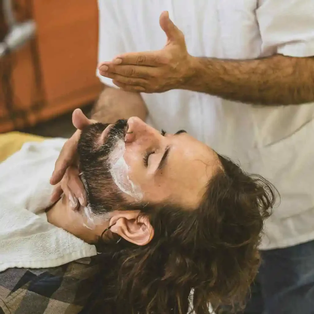 Barber applying shaving cream to a client's face, focusing on a men’s hairstyle undercut.