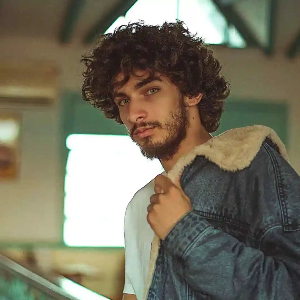 A man with curly hair wearing a denim jacket, showcasing a stylish men's short curly haircut.