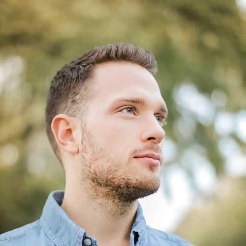 Man in a blue shirt with short hair and a men’s hairstyle undercut, outdoors with blurred greenery in the background.