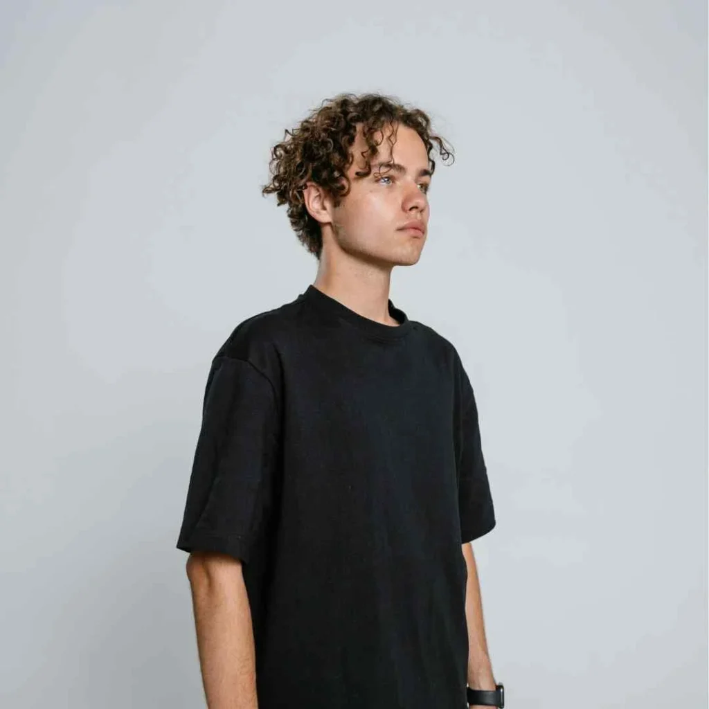 A young man with curly hair wearing a black t-shirt, sporting a stylish men's short curly haircut.