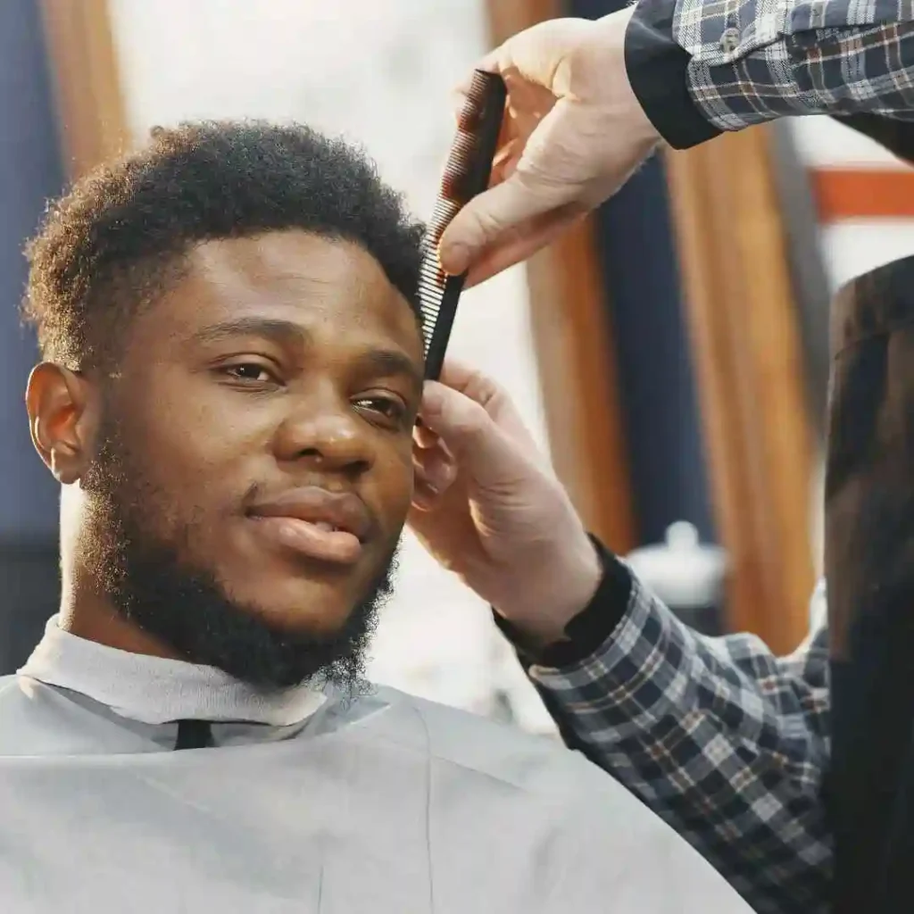 A man getting his hair cut at a barber shop, focusing on his men's short curly haircut being styled.