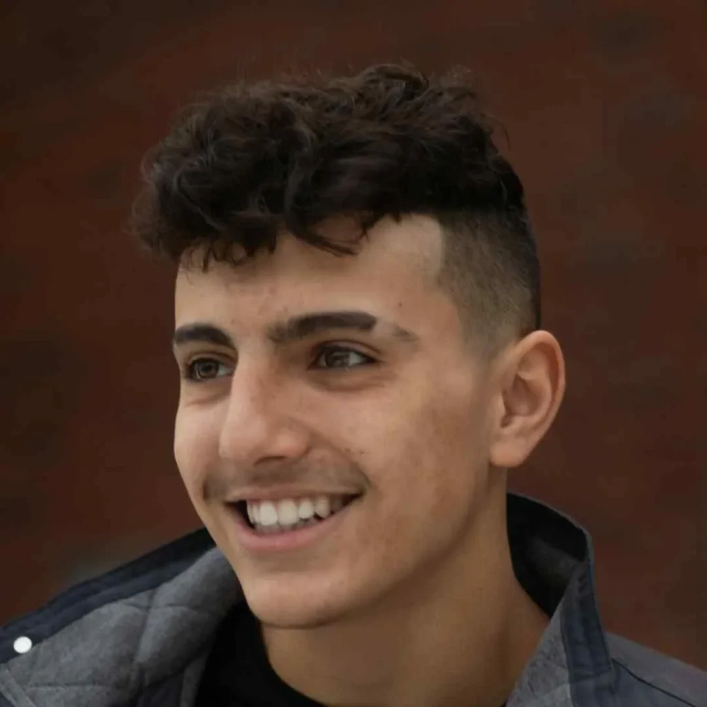 A young man with curly hair smiling at the camera, showcasing a trendy men's short curly hairstyle.