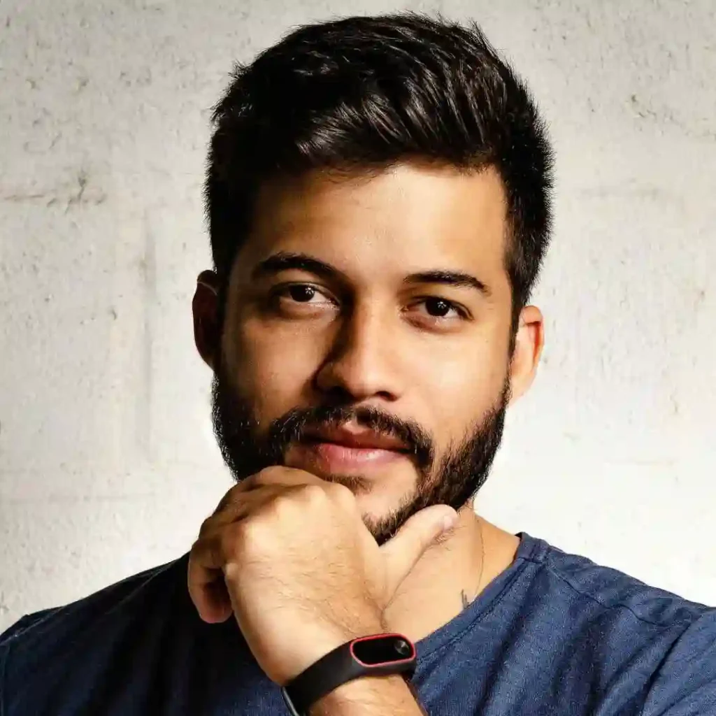 Person in a blue shirt with a fitness tracker on their wrist, featuring a men’s hairstyle undercut, against a white wall.