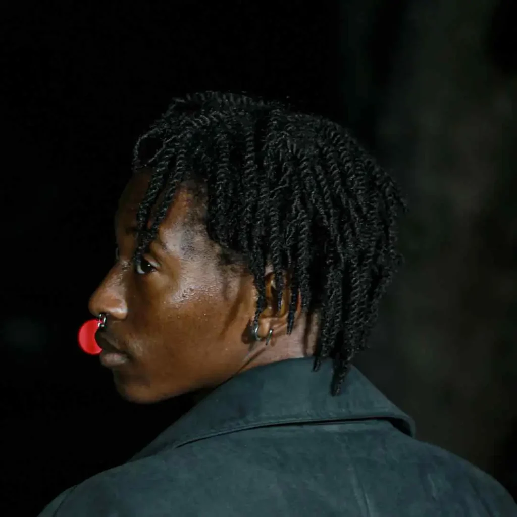 A man with a red nose ring on his nose, styled with a modern men's short curly haircut.