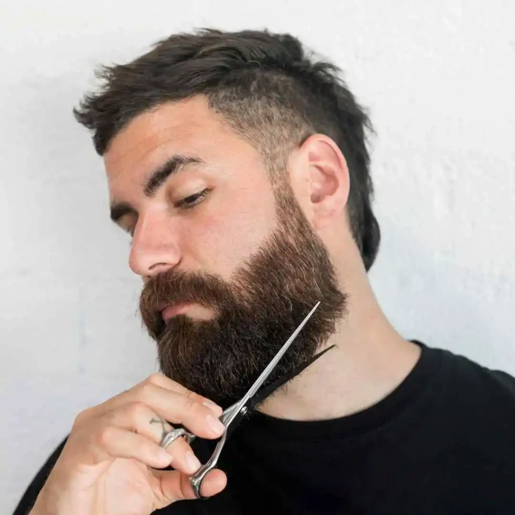 a man with a beard cutting his hair with a pair of scissors