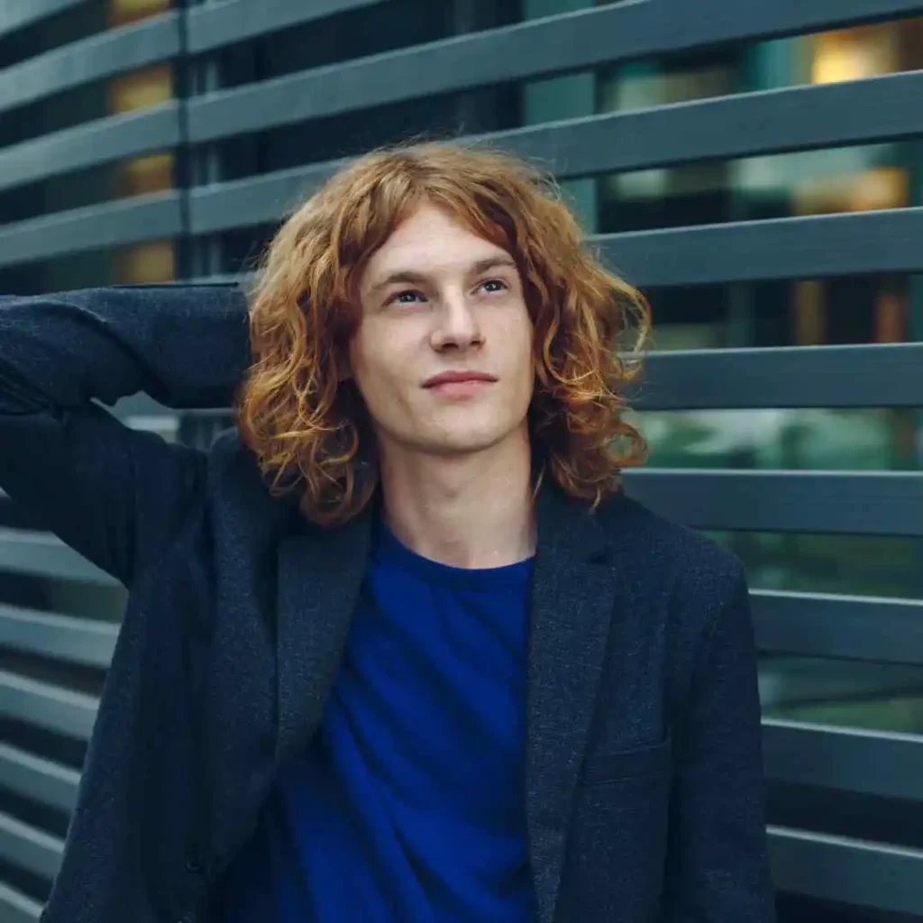 a man with long red hair standing in front of a building