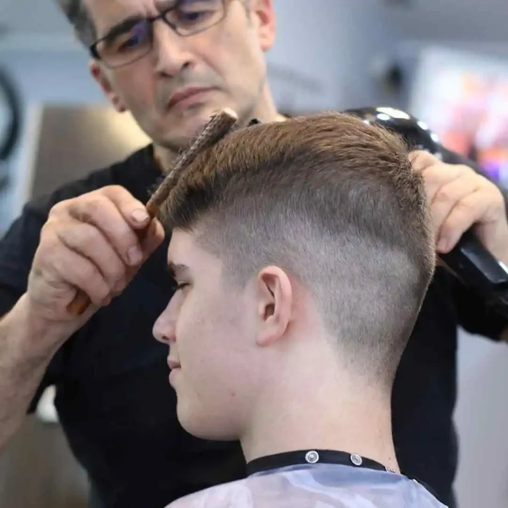 A man getting his hair cut by a barber, showcasing a fade hairstyles for men as the barber works on the sides and shapes the top.