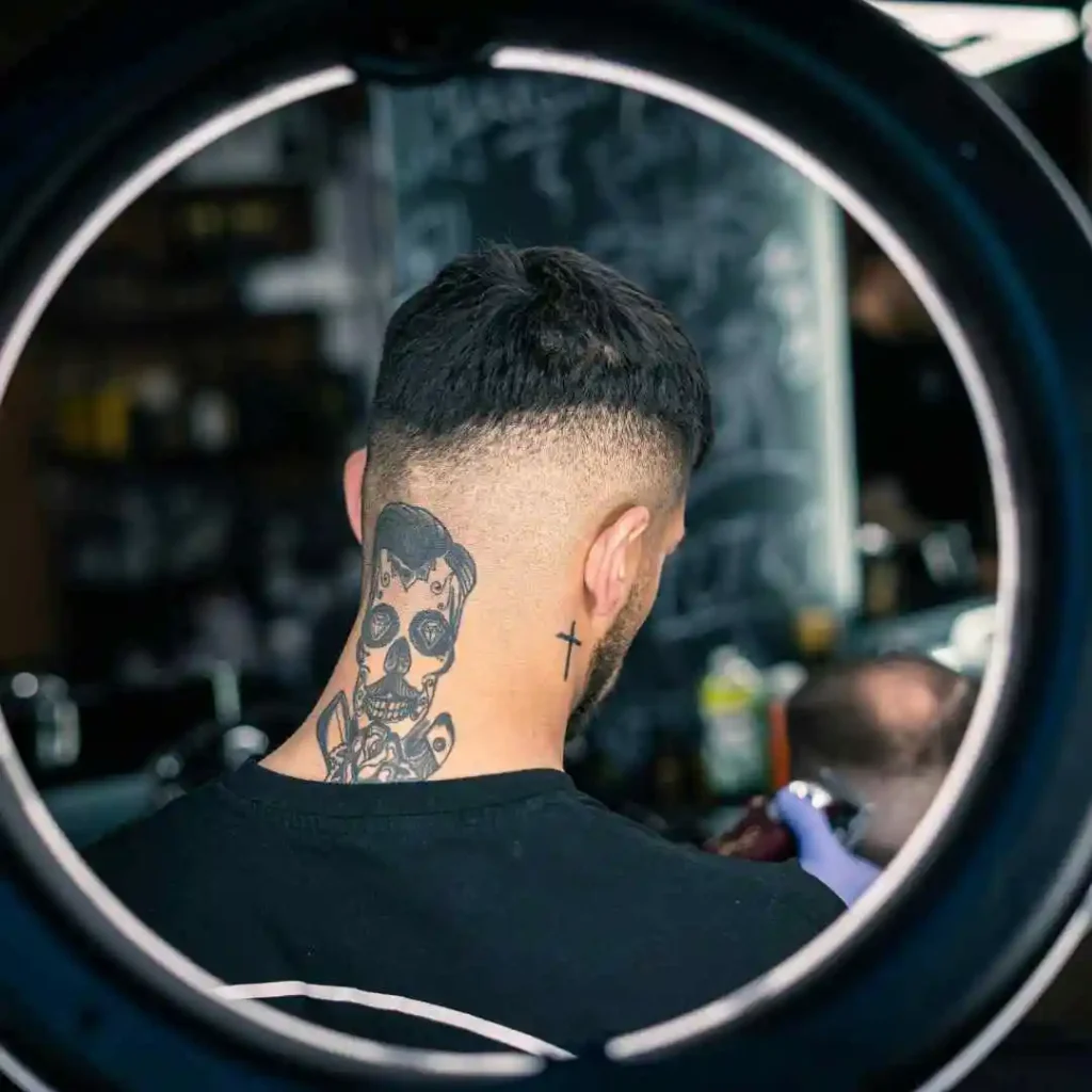 A man with a skull tattoo on his neck, wearing fade hairstyles for men, with the sides neatly faded and the top styled.