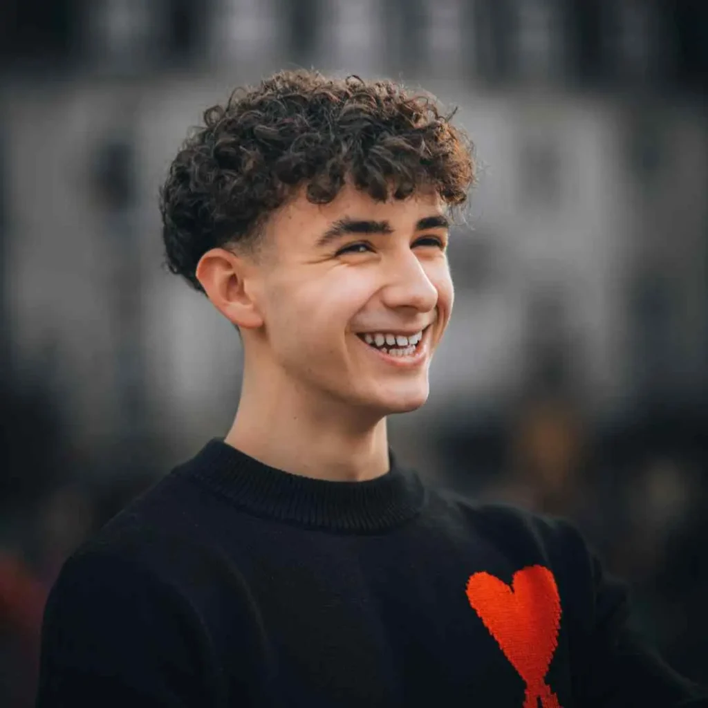 a young man with curly hair smiles at the camera