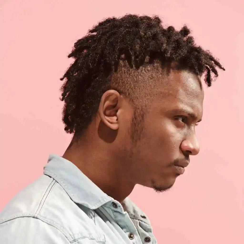 Person with short curly hair in a light blue shirt against a pink background.