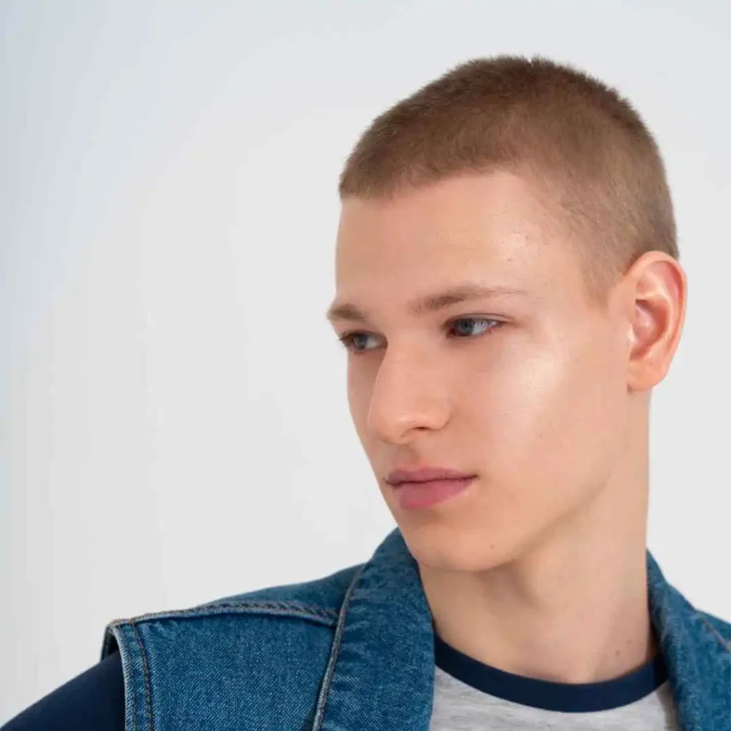 Person with short hair wearing a denim jacket over a grey shirt, against a white background, showcasing men hairstyles for oval face.