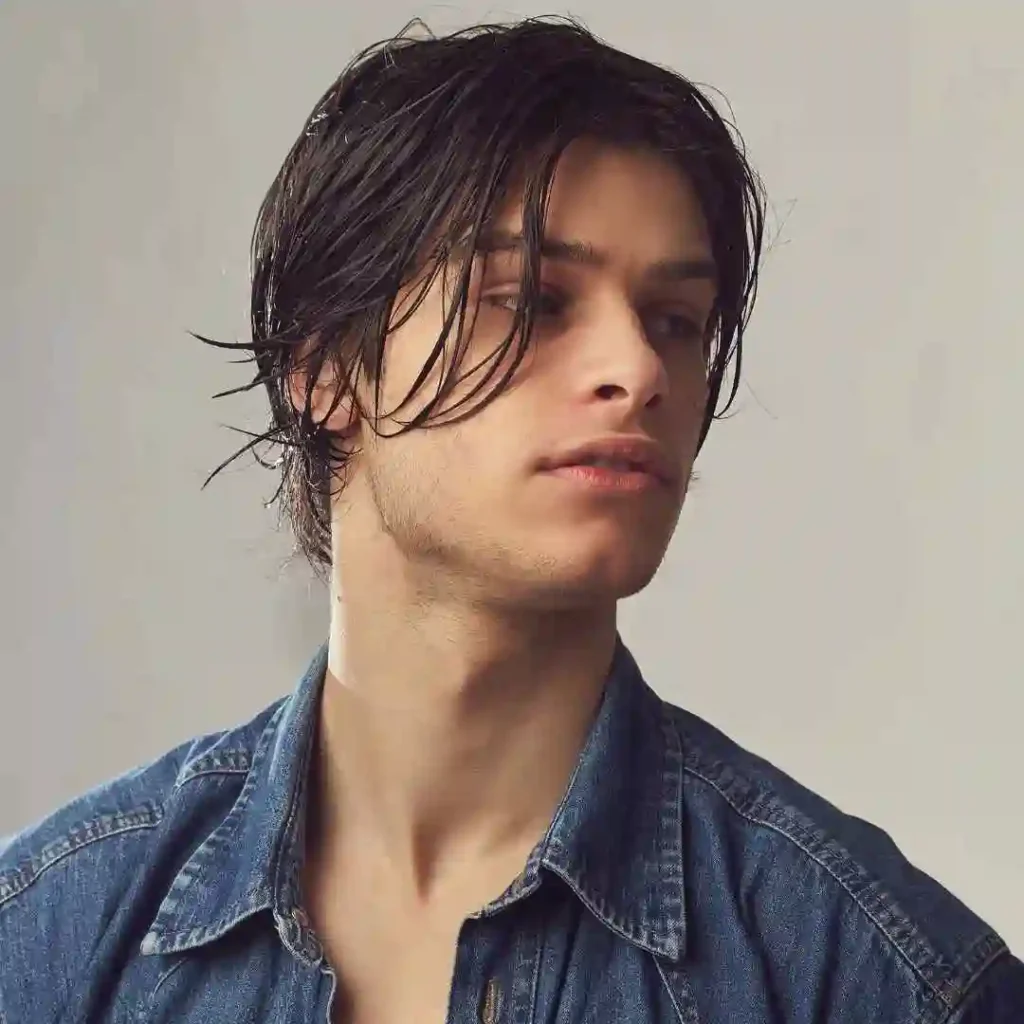 Person with wet hair wearing a denim shirt, against a grey background.