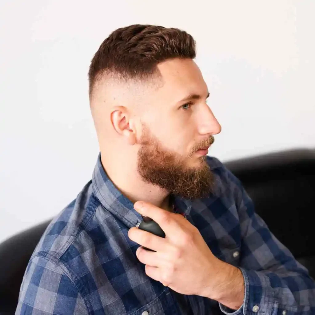 Man in a plaid shirt trimming his beard with an electric clipper.