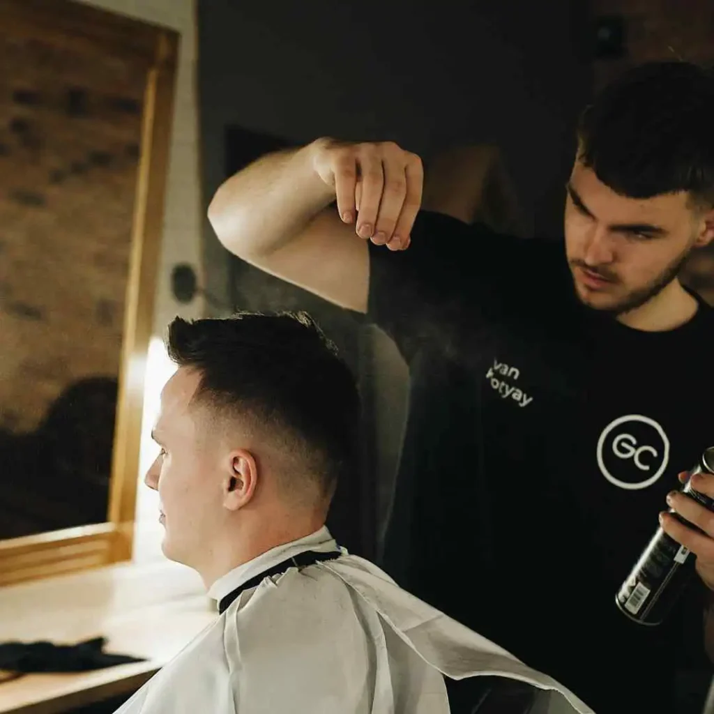 Barber using hairspray on a client's styled haircut.