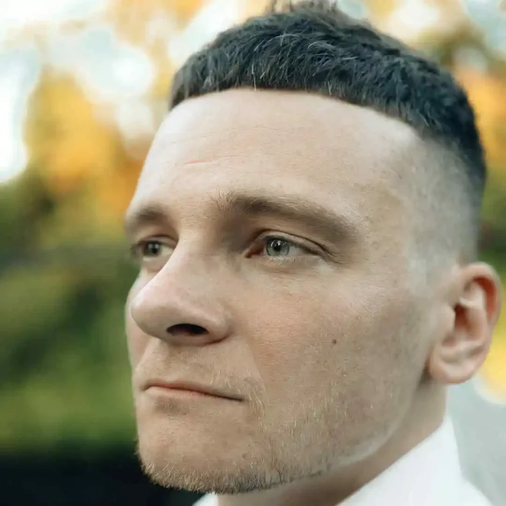 Rear view of a person with a short haircut against a blurry autumnal background.