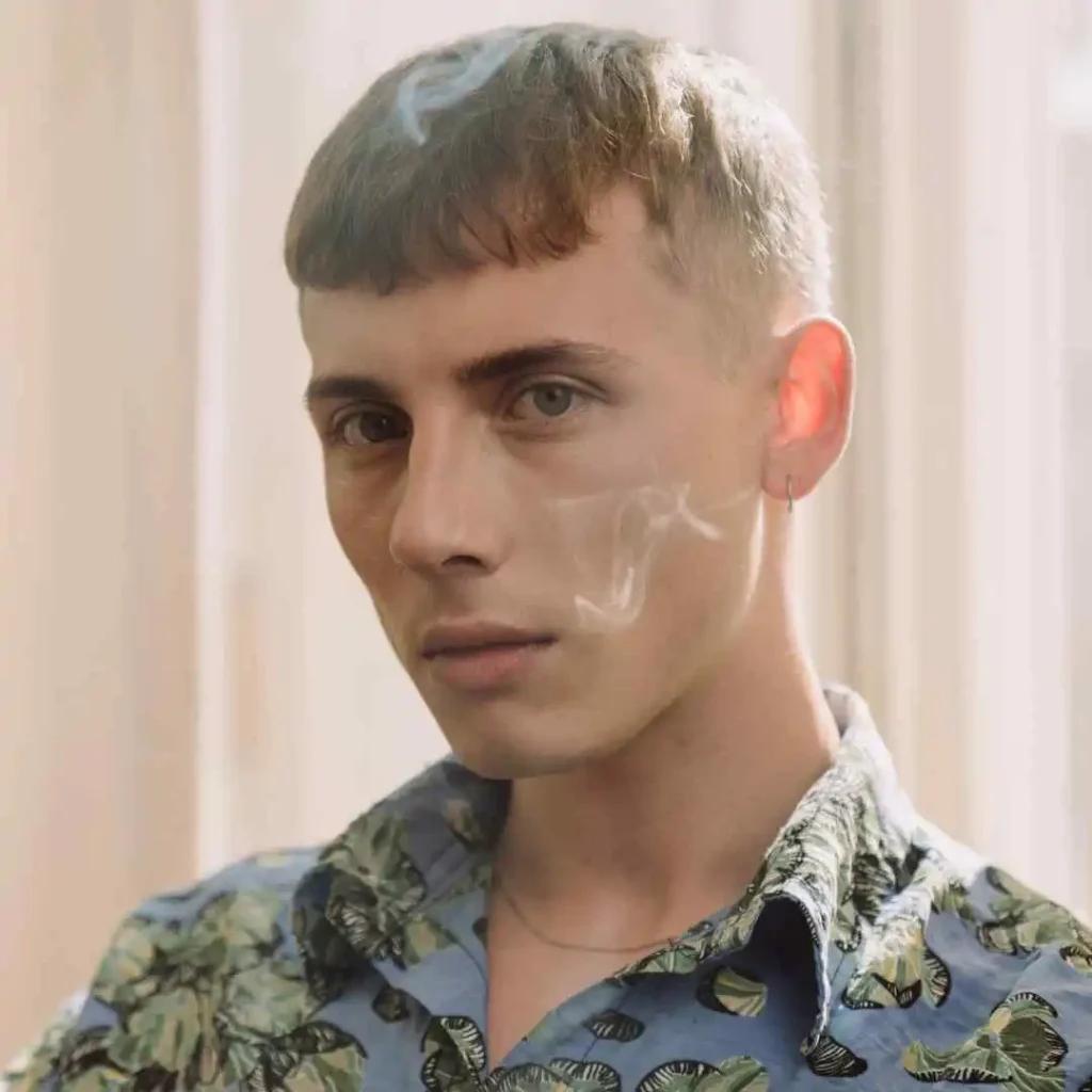 A man with a cigarette in his mouth, showcasing haircuts for men with diamond face.