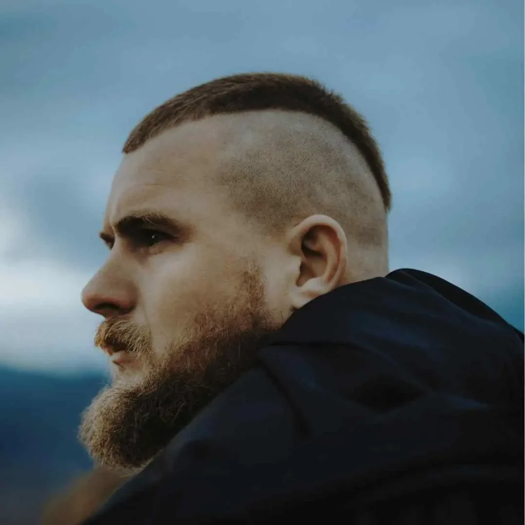 Rear view of a person with a short haircut against a soft blue sky background.