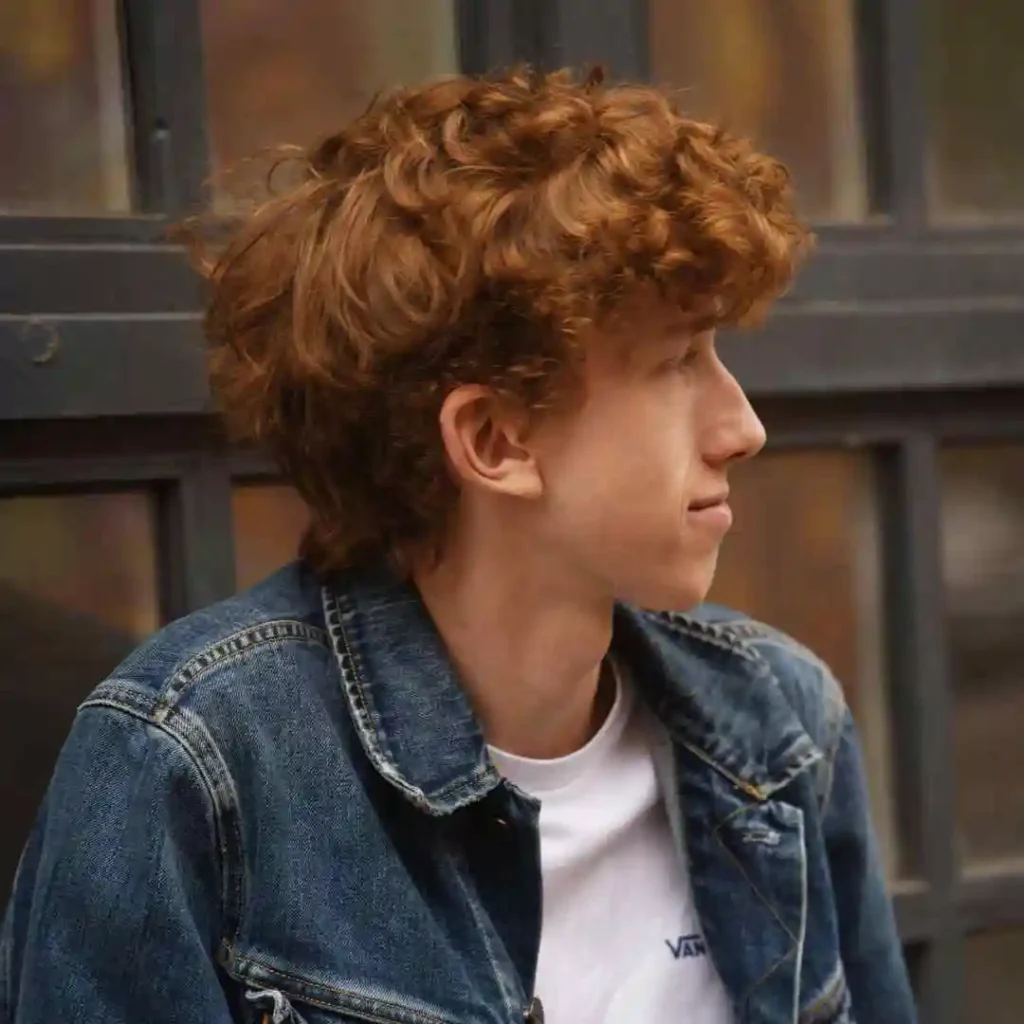 Person with curly hair wearing a denim jacket and white T-shirt.