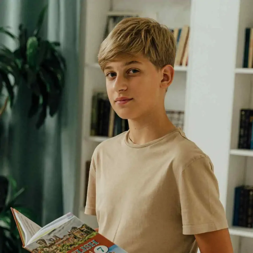 Person holding a book in a room with bookshelves and a plant.