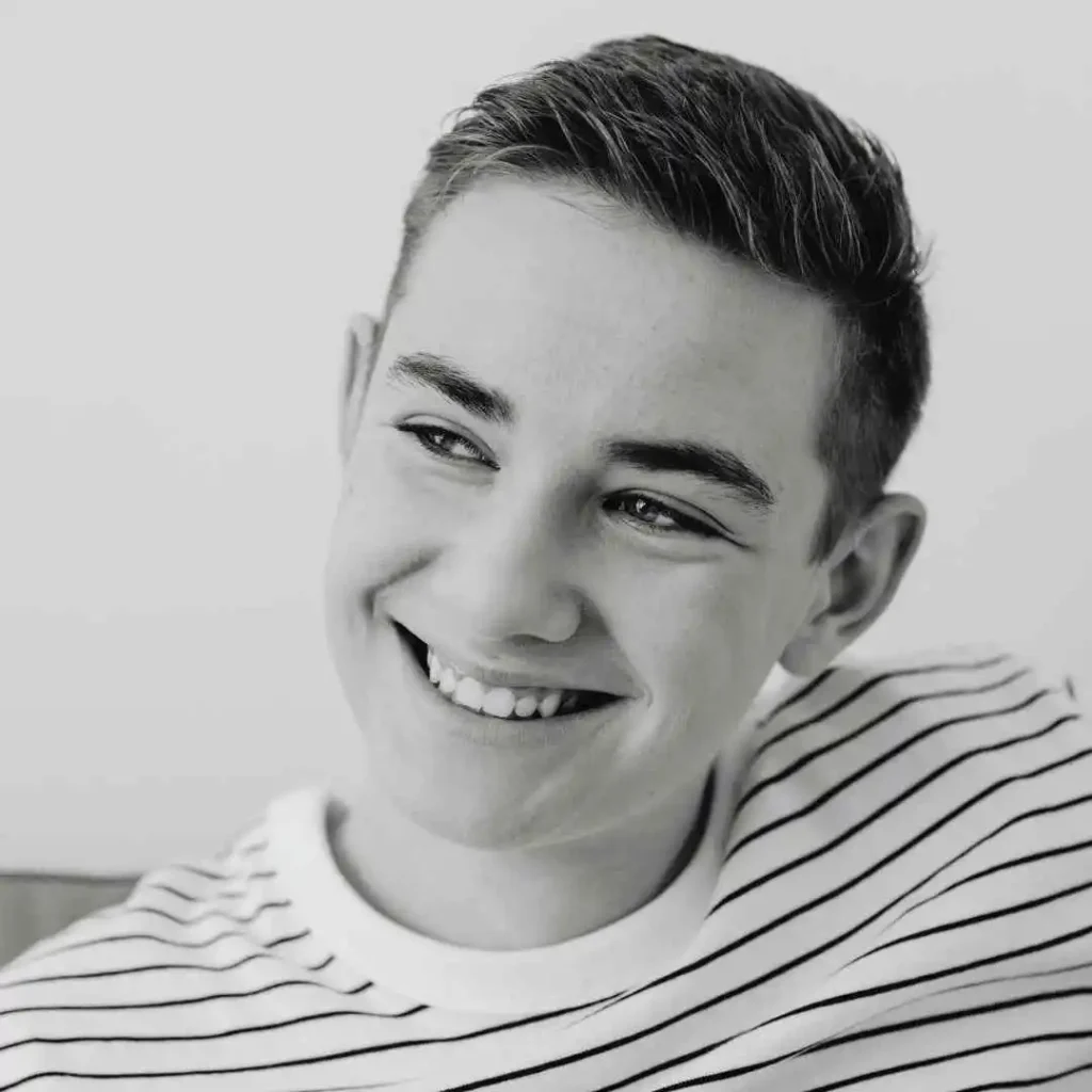 A young man smiling in a black and white photo, showcasing haircuts for men with diamond face.