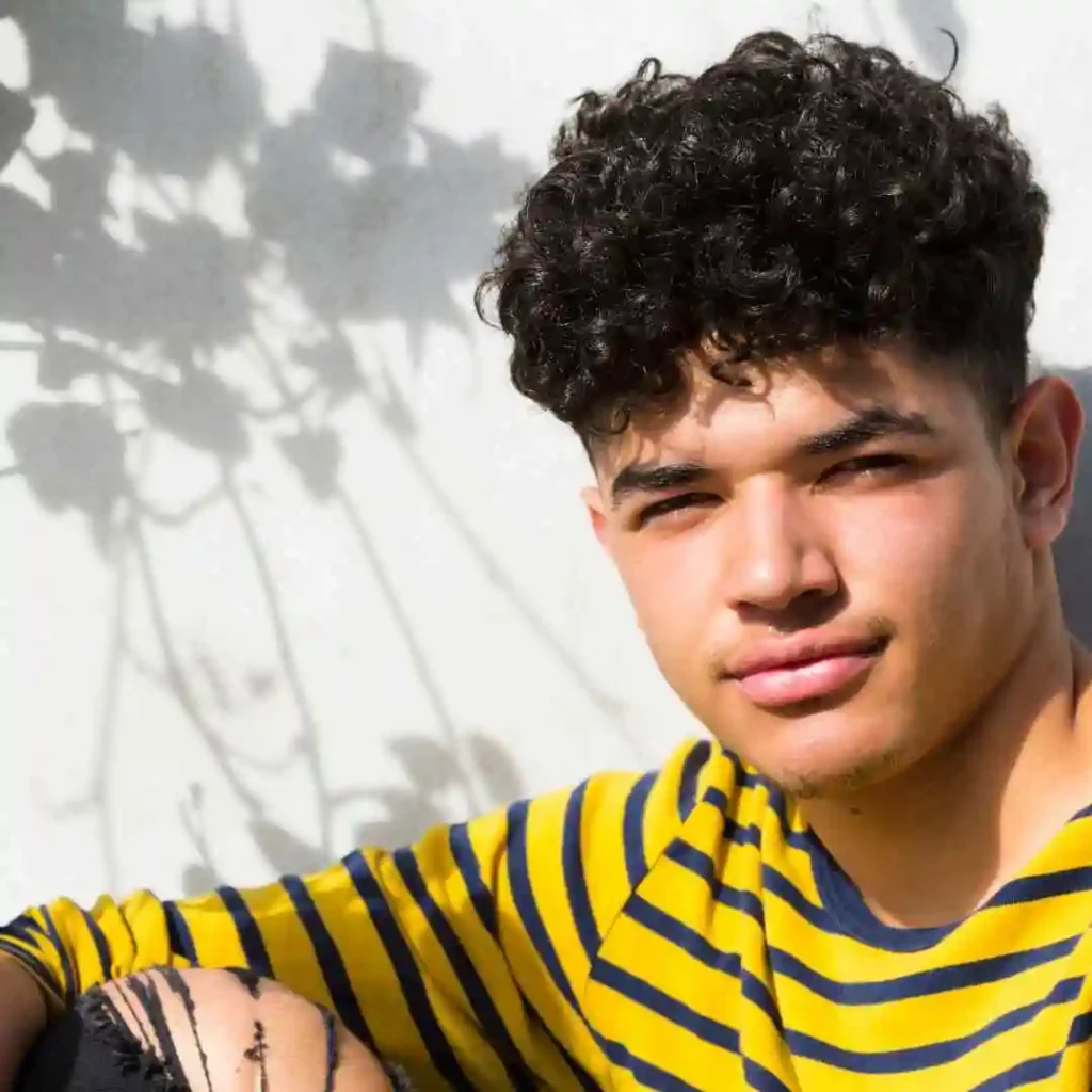 Back view of a person with curly hair wearing a striped shirt, with plant shadows on the wall.