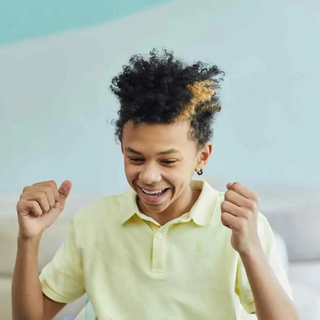 Person in yellow polo shirt with curly hair, gesturing with fists in excitement.