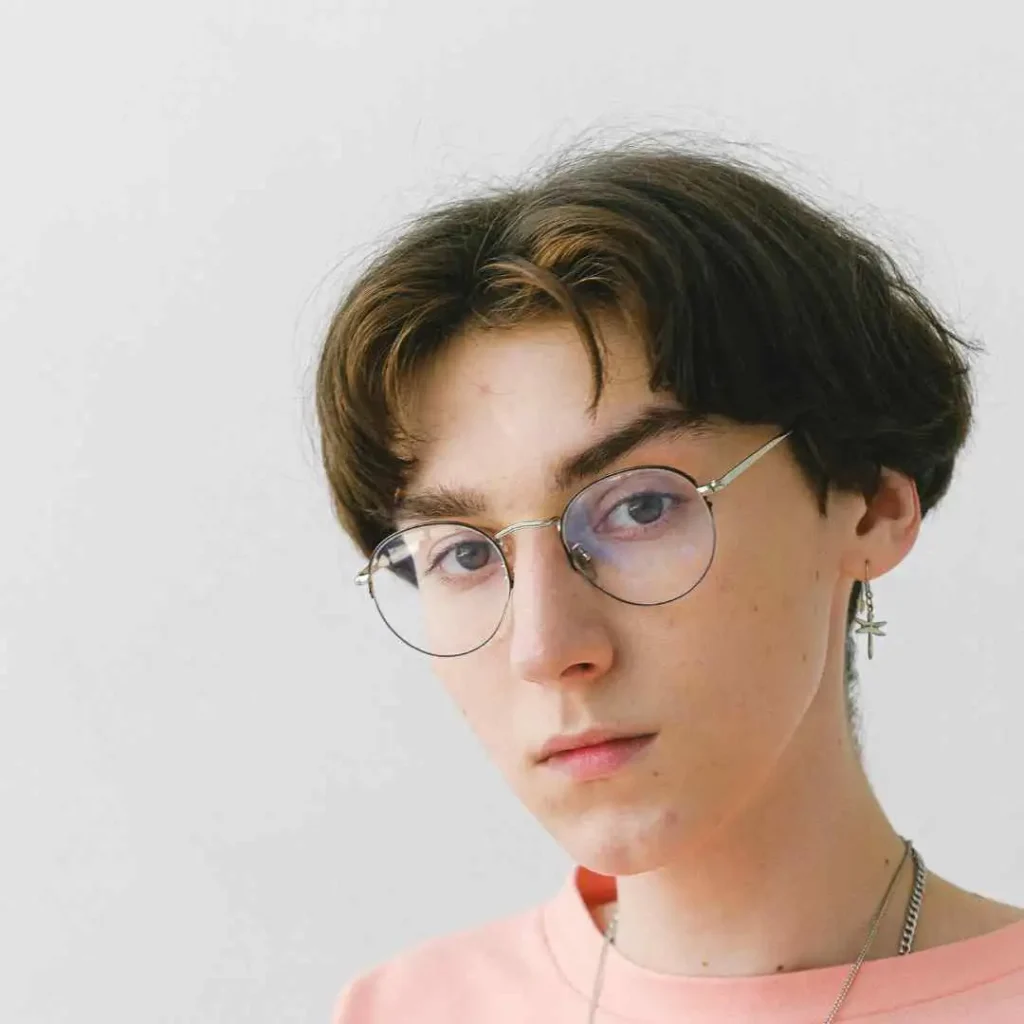 Person with dark hair, earrings, and a pink shirt against a white background.