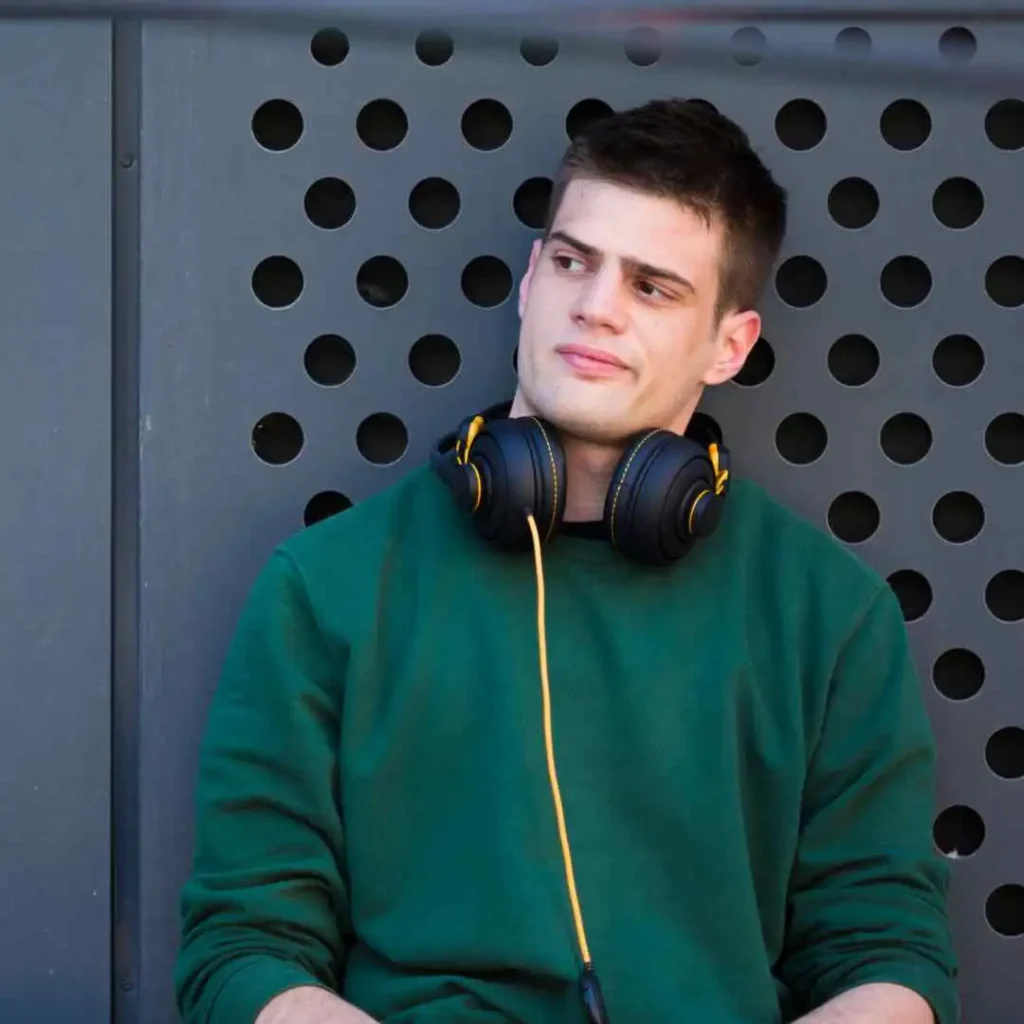 Person in a green hoodie with headphones around neck against a perforated background.