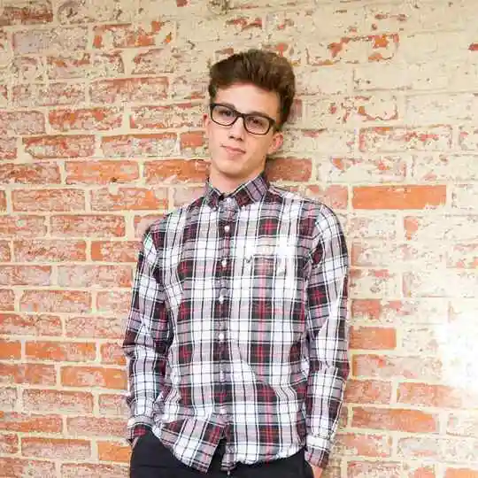 Person in a plaid shirt standing against a brick wall.