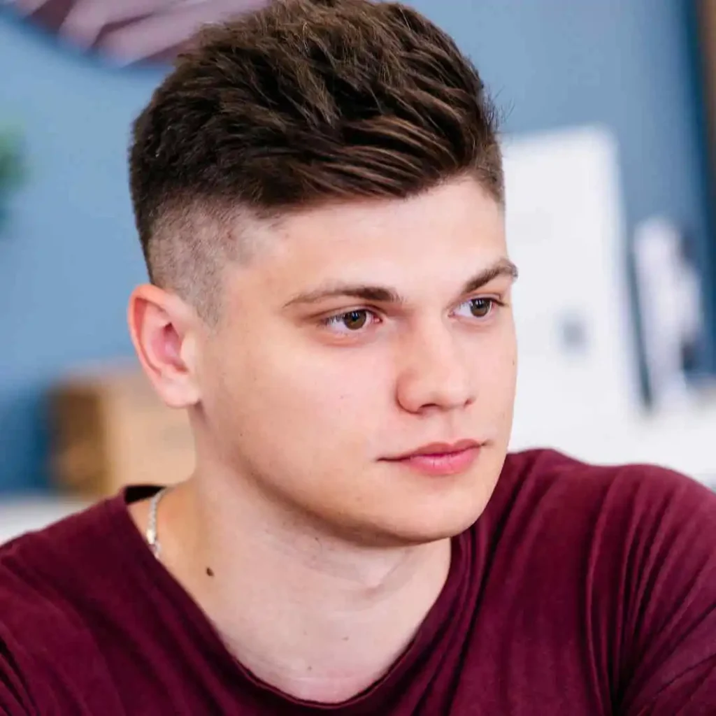 Person in a burgundy shirt with a modern hairstyle, indoors.