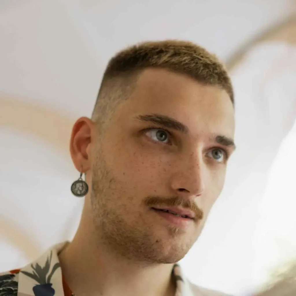 Individual with a buzz cut and an earring, wearing a floral shirt.