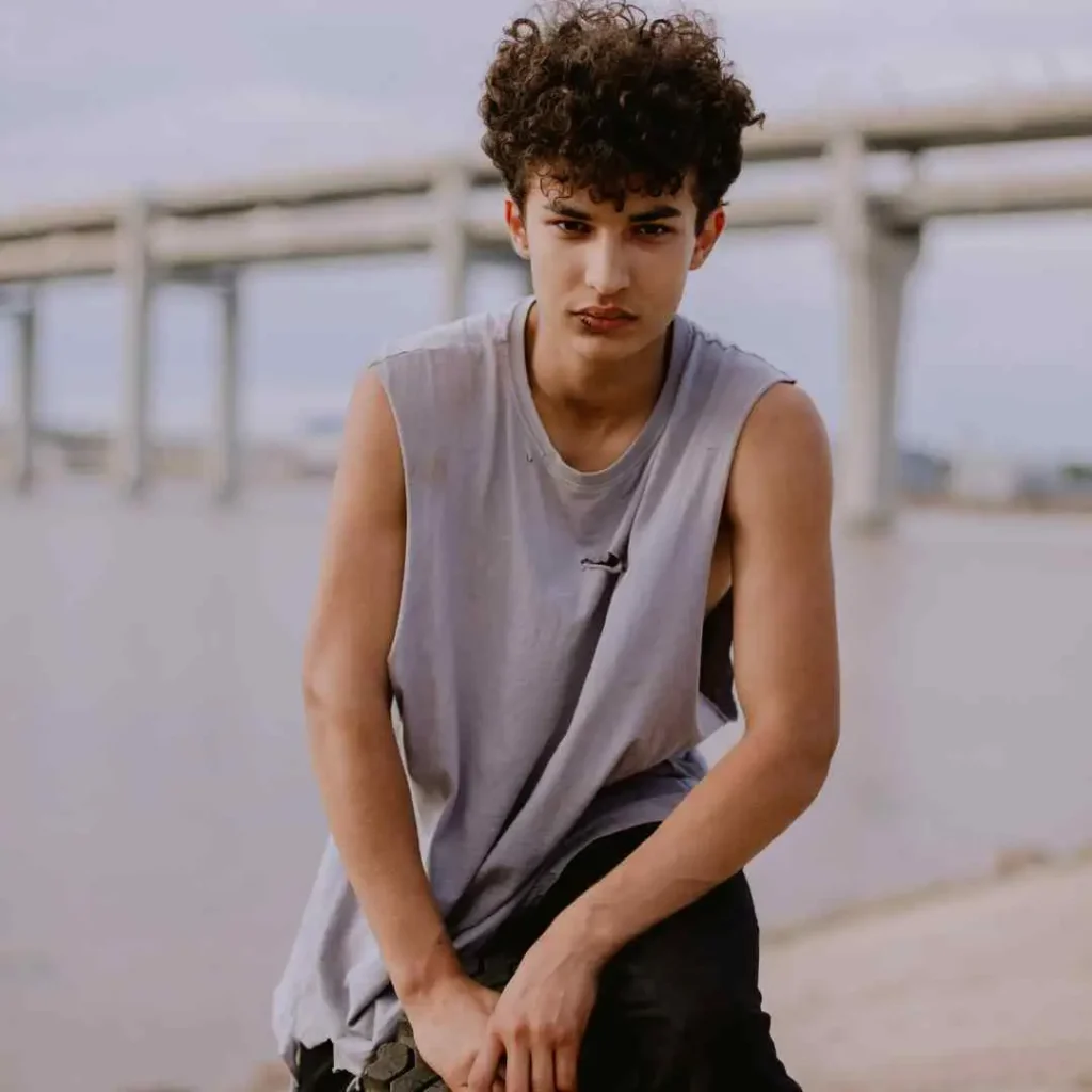 Person in a sleeveless top sitting with hands clasped, with a bridge in the background.