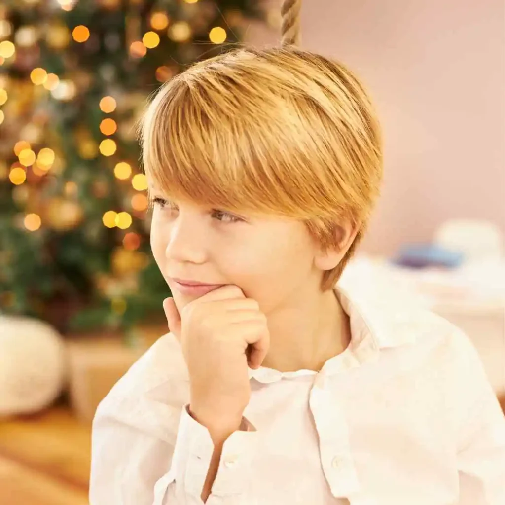 Child in a white shirt with a Christmas tree in the background.