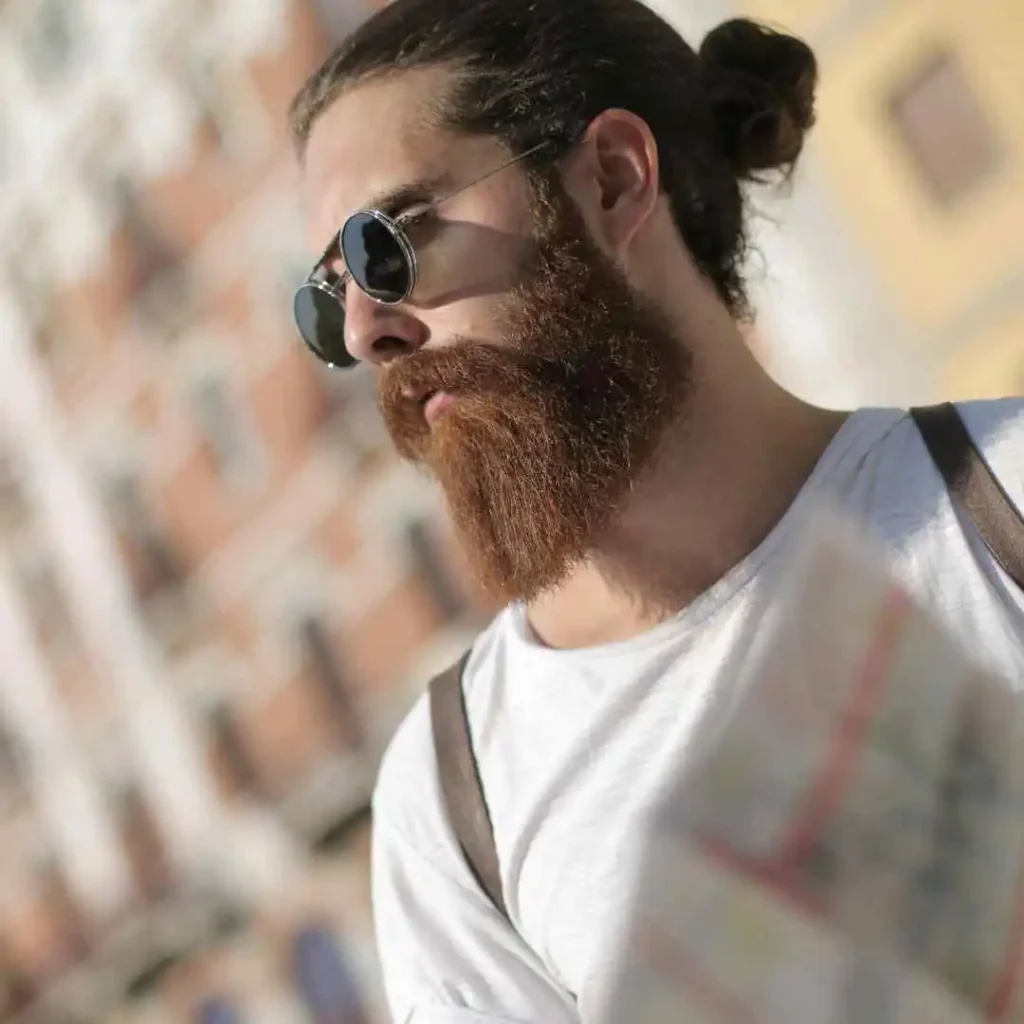 Man with beard and man bun wearing a gray t-shirt with urban background.