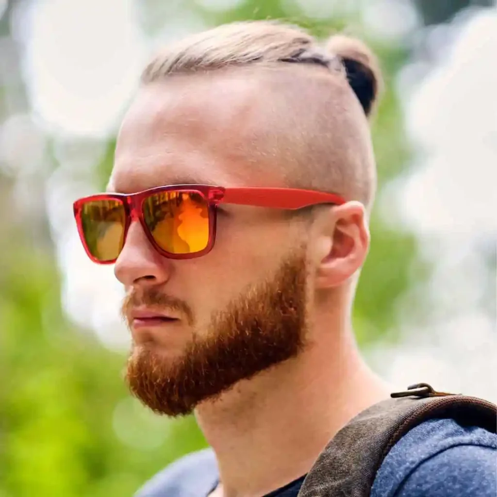 Person with undercut hairstyle wearing red sunglasses and a backpack outdoors.