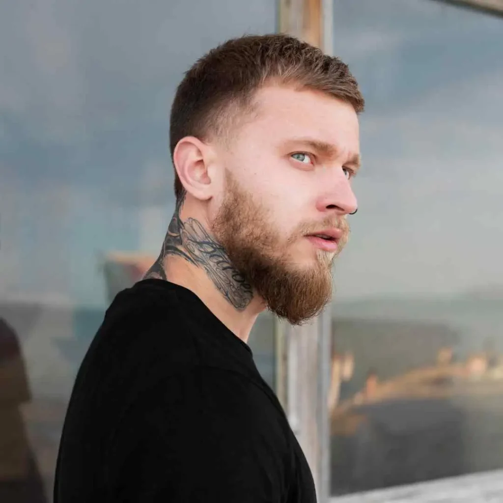 Side profile of a person with a neck tattoo and short hair, wearing a black shirt.