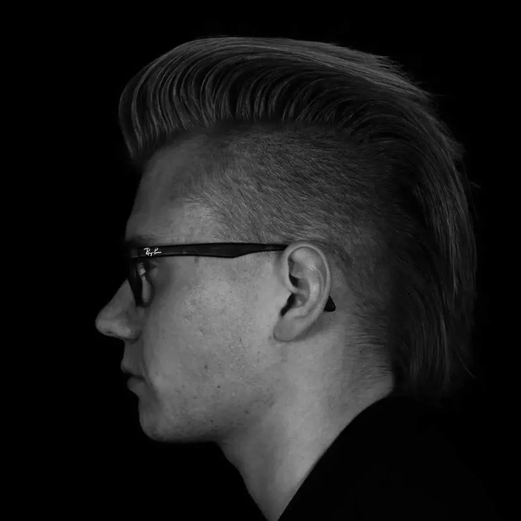 Profile view of a person with a slicked-back hairstyle, in monochrome against a black background, featuring a sleek and modern Mohawk men hairstyle.