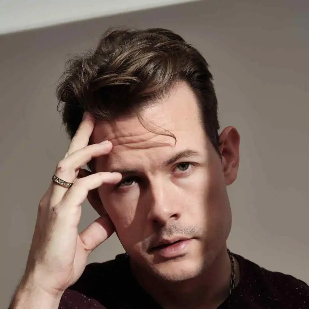 A man is holding his hand to his head, showcasing haircuts for men with diamond face.